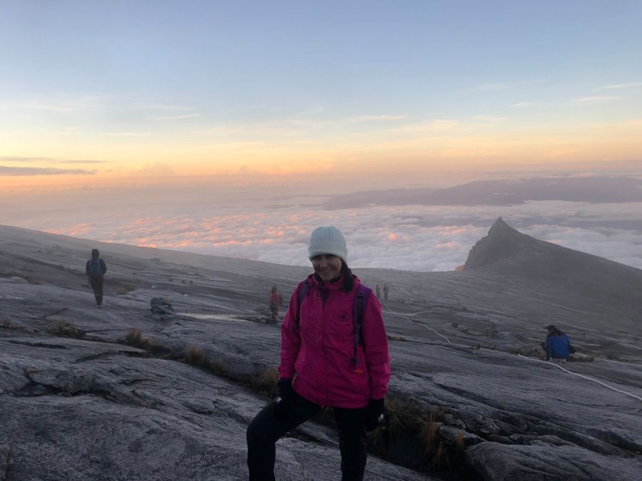 Sahar smiling near the summit of Mount Kinabalu at sunrise, above a sea of clouds